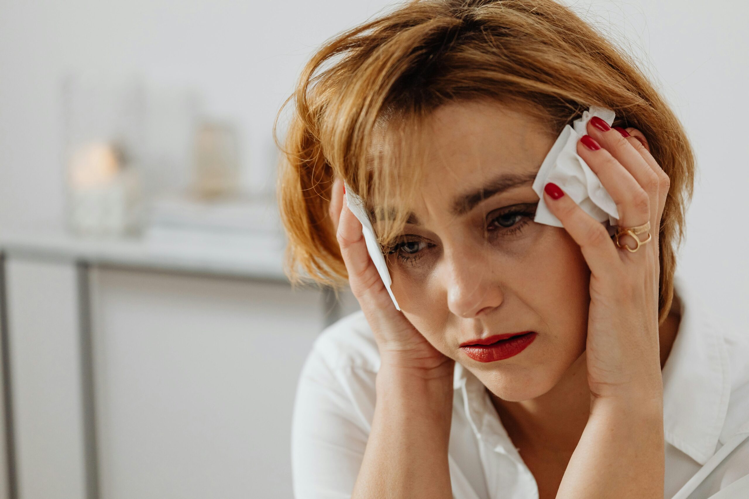 Exhausted woman sitting in stillness, holding tissue to her head in grief.