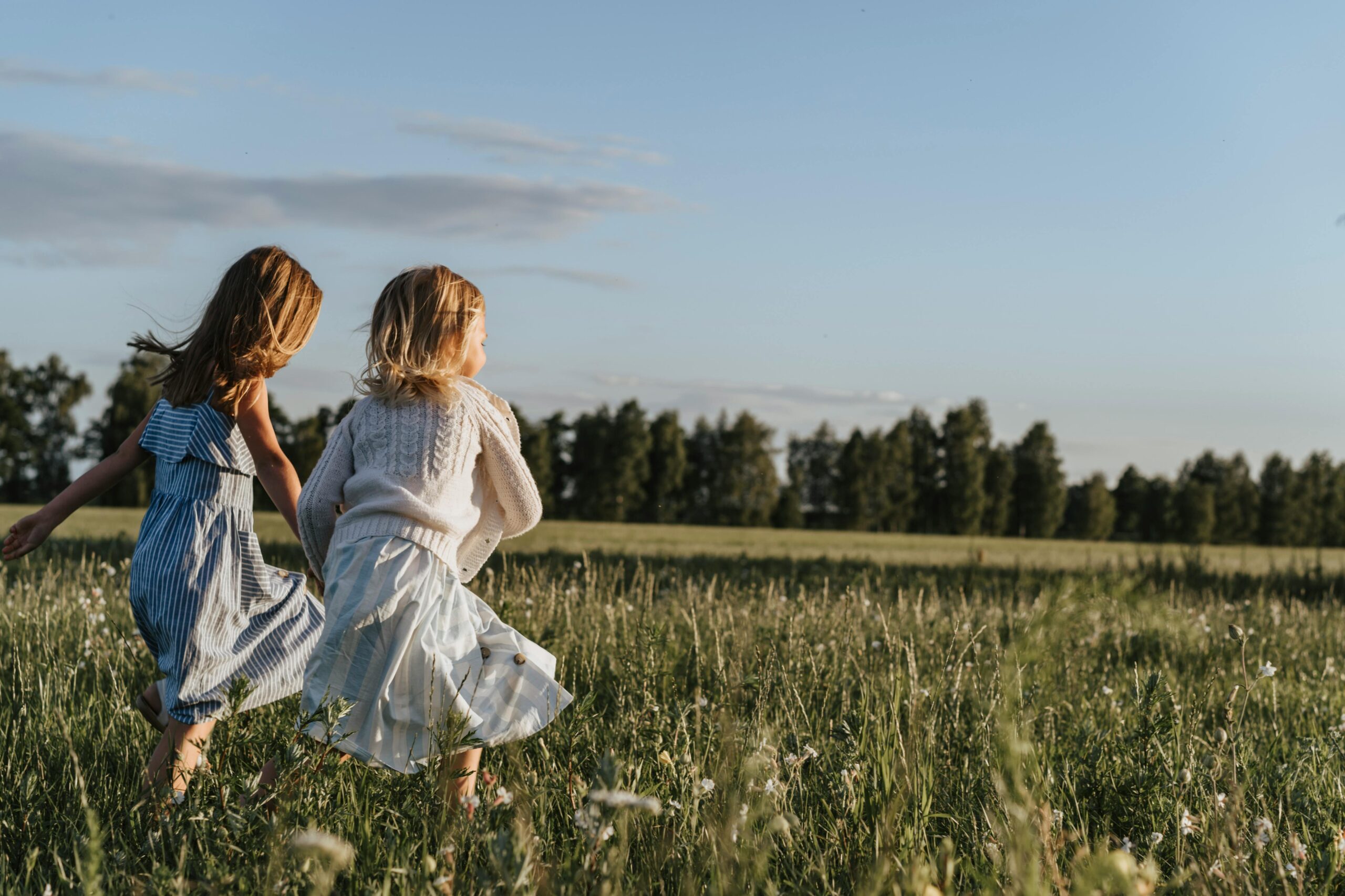 Two young girls running through a sunlit field, evoking the innocence, vulnerability, and emotional conditioning we carry from childhood into adult love.